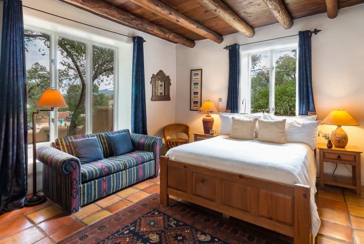 Bedroom with Saltillo tile floor, blue drapes on expansive windows, bed made up in white and southwestern-style sofa.