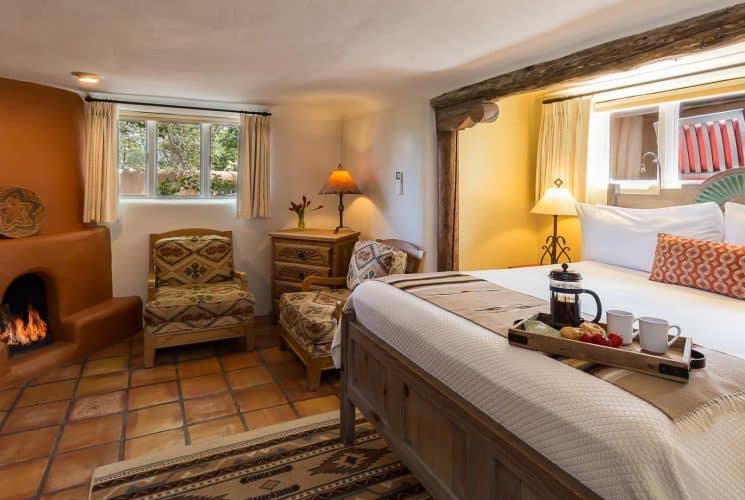 Plaster fireplace in bedroom with Saltillo tile floor, seating area and king-size bed inset cleverly into the wall.