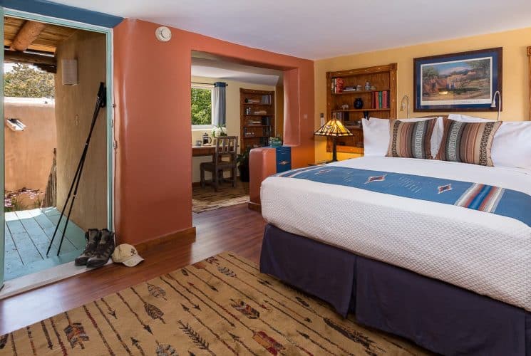 Bedroom with blue, cream and terra-cotta painted walls, wooden floors, arrow rug and bed made up in white and blue.