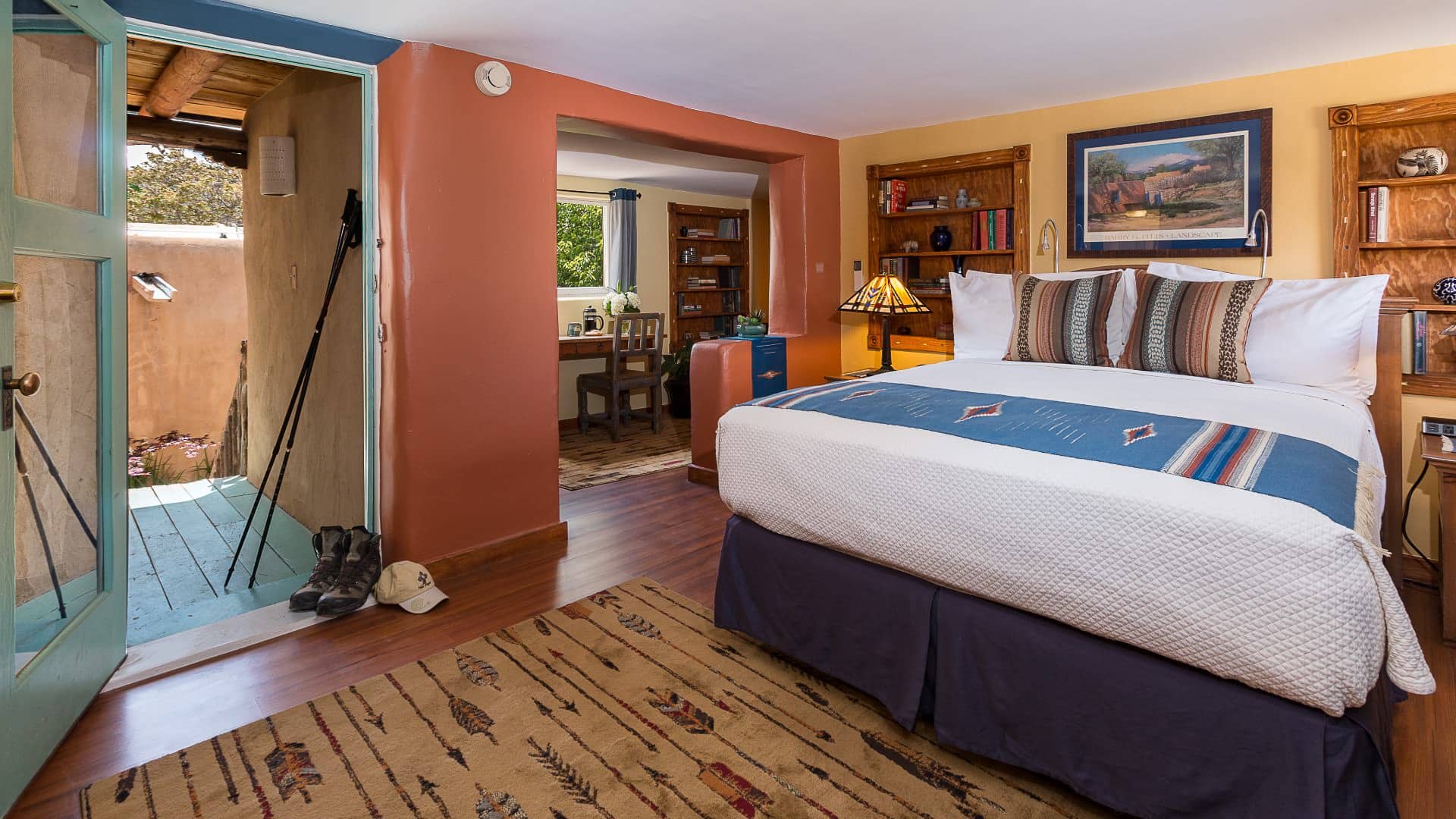 Bedroom with blue, cream and terra-cotta painted walls, wooden floors, arrow rug and bed made up in white and blue.