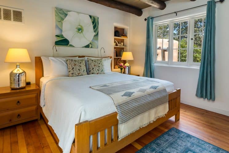 Bed with white bedding in room with plastered walls, beams in ceiling, Quaker-style furniture and Georgia O'Keefe print.