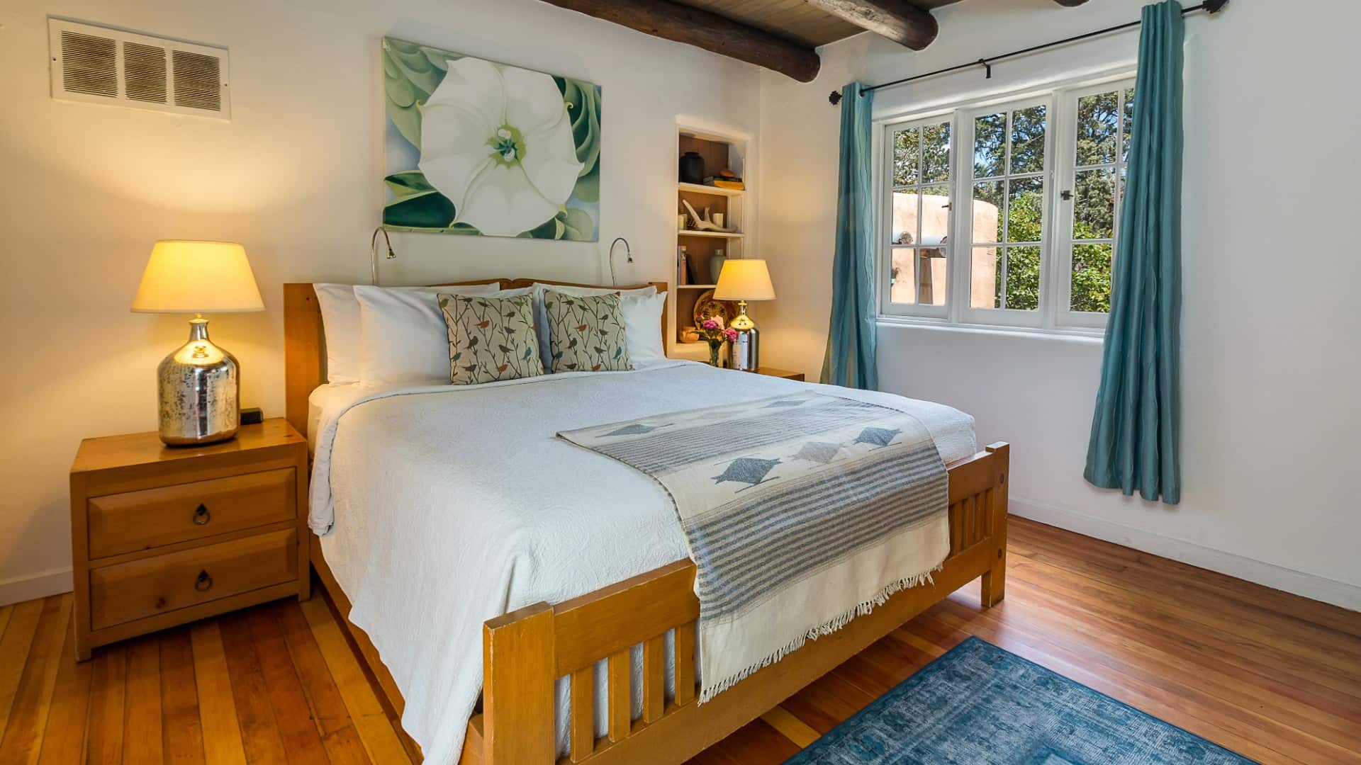 Bed with white bedding in room with plastered walls, beams in ceiling, Quaker-style furniture and Georgia O'Keefe print.