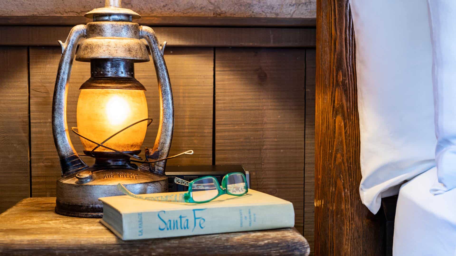 Close up view of wooden nightstand with antique book, antique lantern and green reading glasses