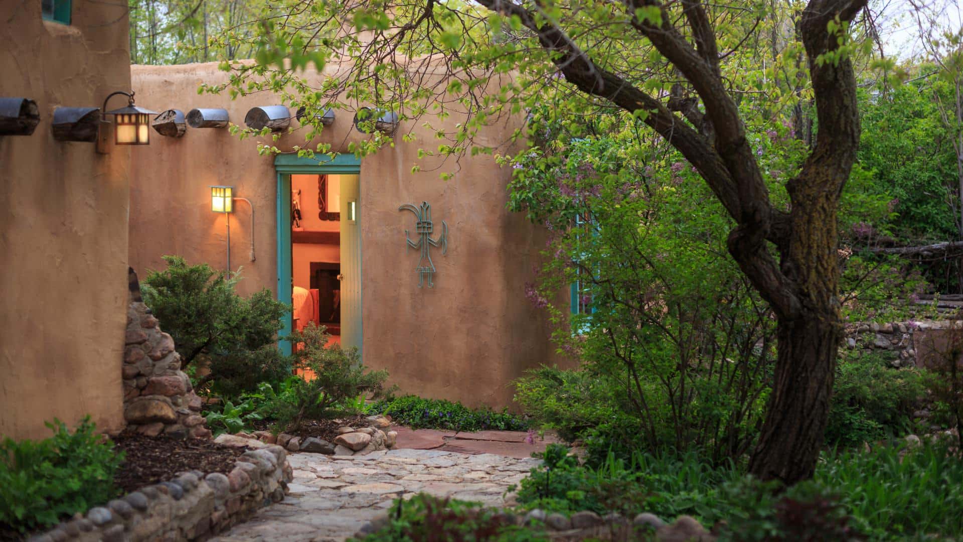 Exterior door to stone walkway from bedroom in tan adobe building with a warrior iron art piece on wall.