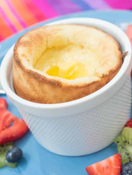 Soufflé in white ramekin on blue plate surrounded by berries and kiwi.