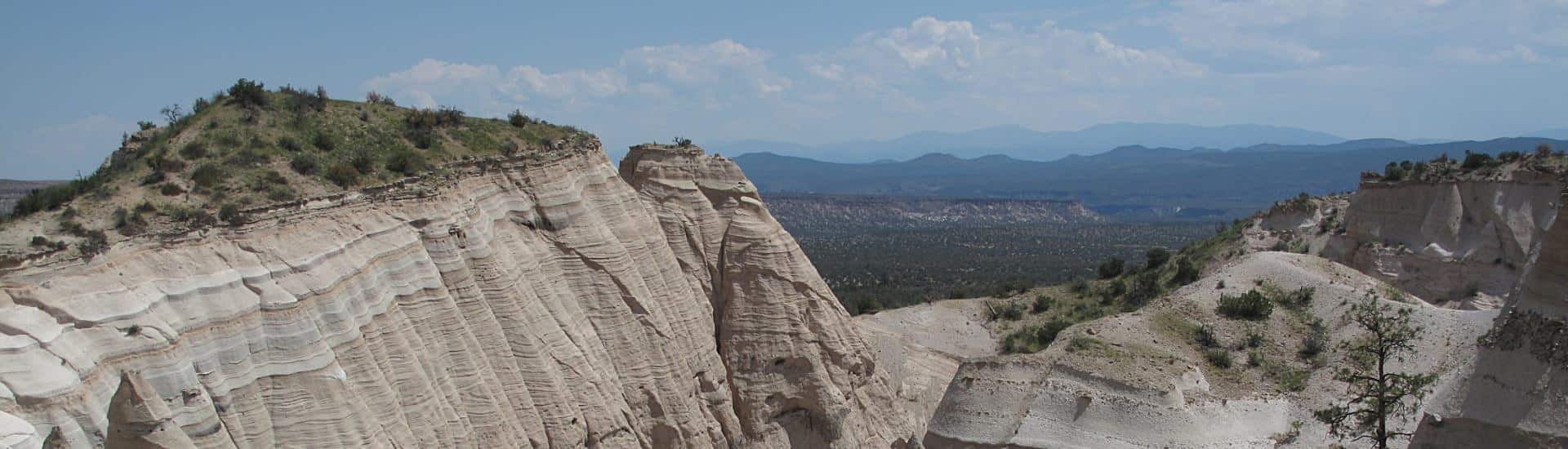White sandstone mountain cliffs topped with scrub overlooking flatland and mountains in the distance.