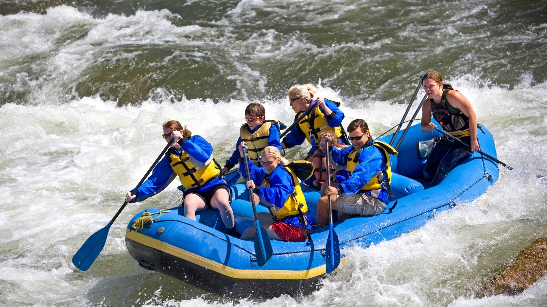 Six people in a blue raft traveling down the white water rapids