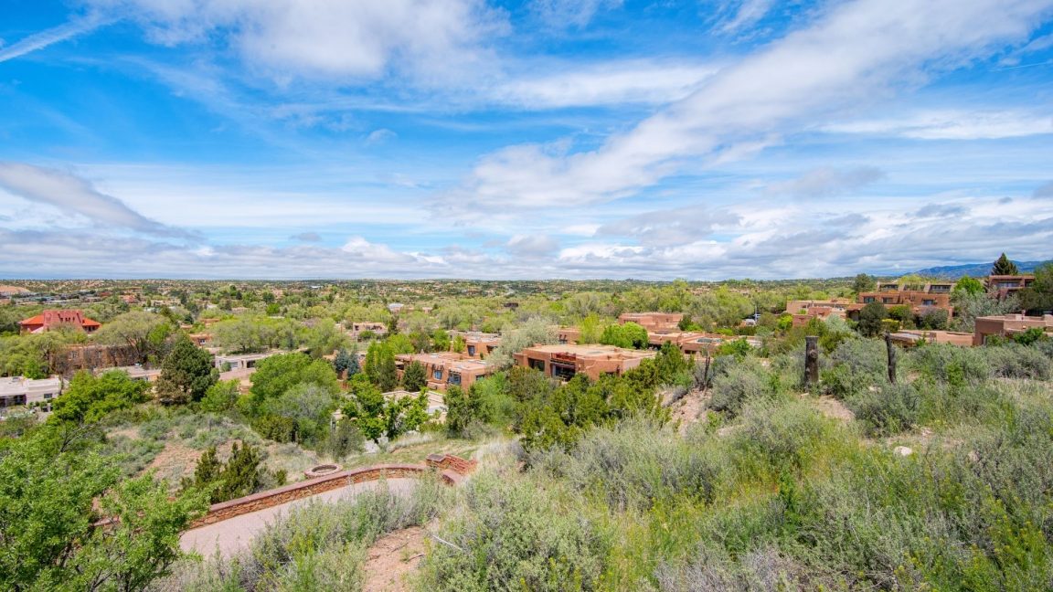 Aerial view of Santa Fe, NM with terra cotta adobe buildings amidst green trees and blue skies