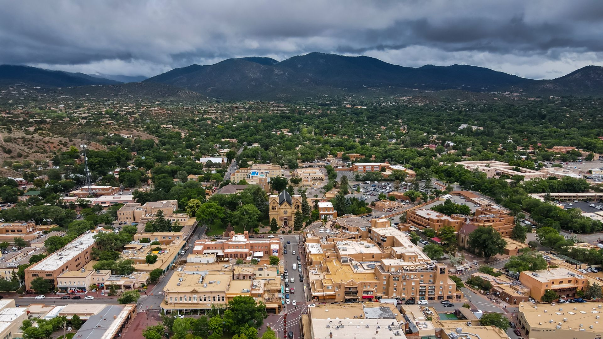 Aerial view of Santa Fe with grids of streets, adobe buildings, and mountains in the background