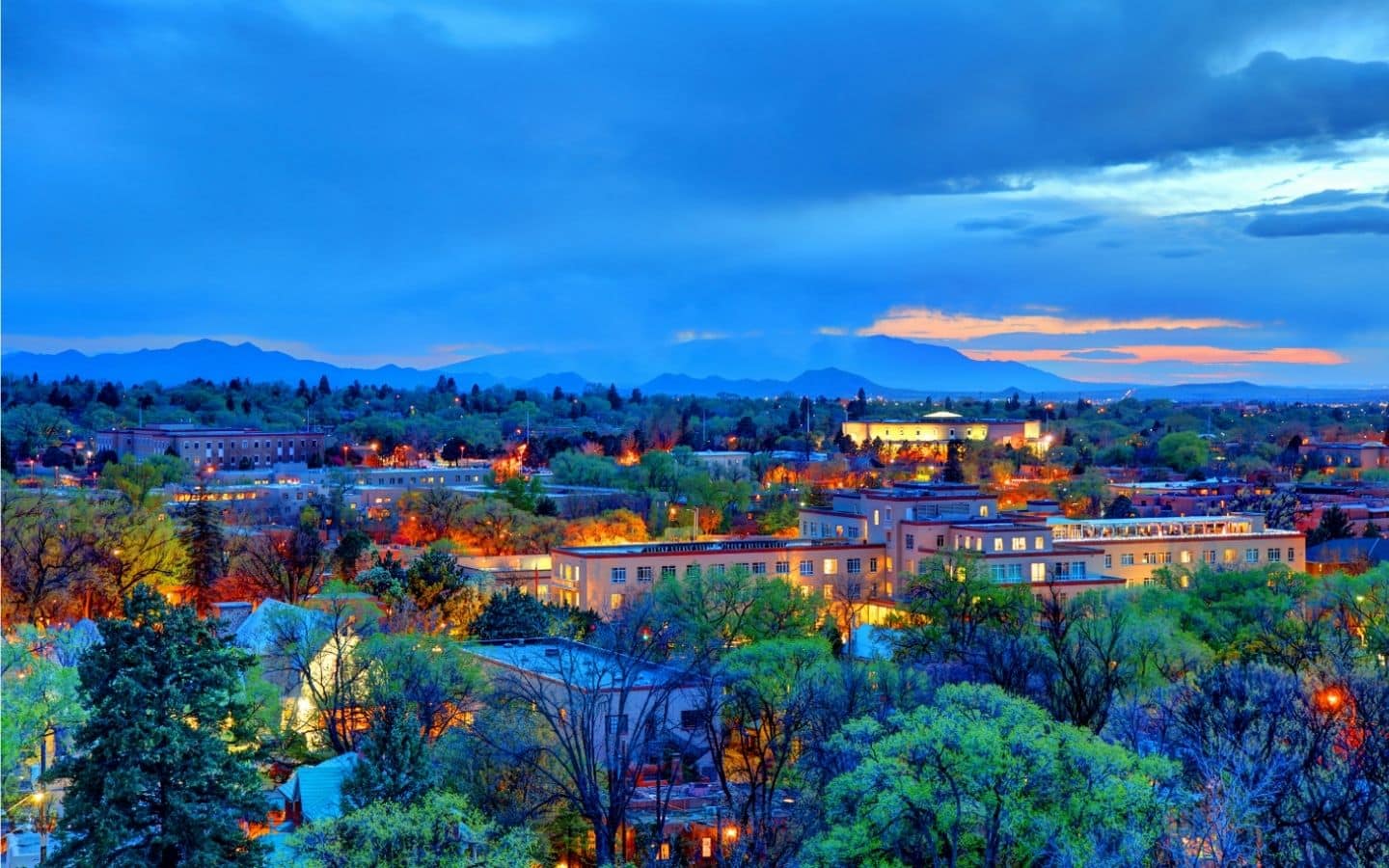 Aerial view of Santa Fe at dusk with lots of warm lighting and pastel colors|Mixologist serving drinks at the bar at Radish and Rye restaurant|seating area in atrium area at Herve Wine Bar in Santa FE|Couple at snow skiing at top of mountain ski santa fe