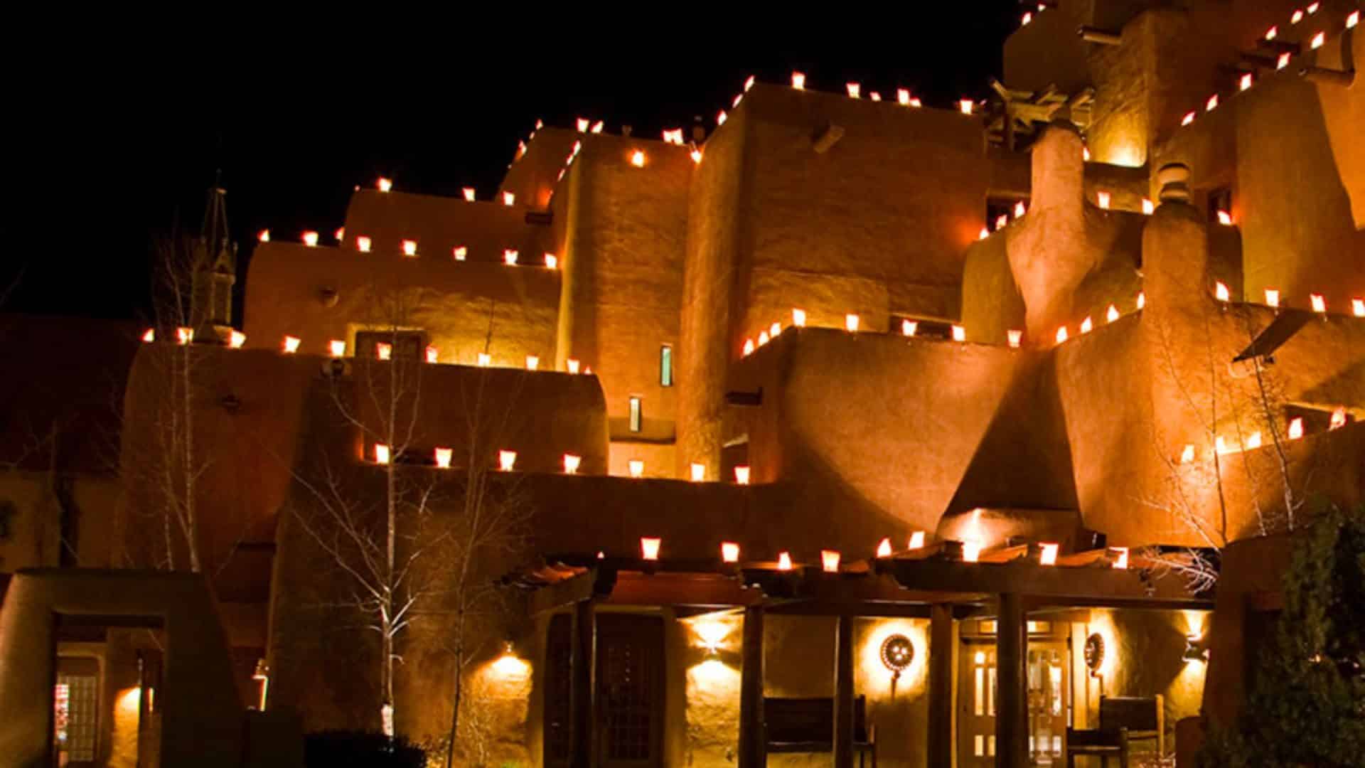 Multi-story, historic adobe building in santa fe dressed in layers of lit up farolitos.