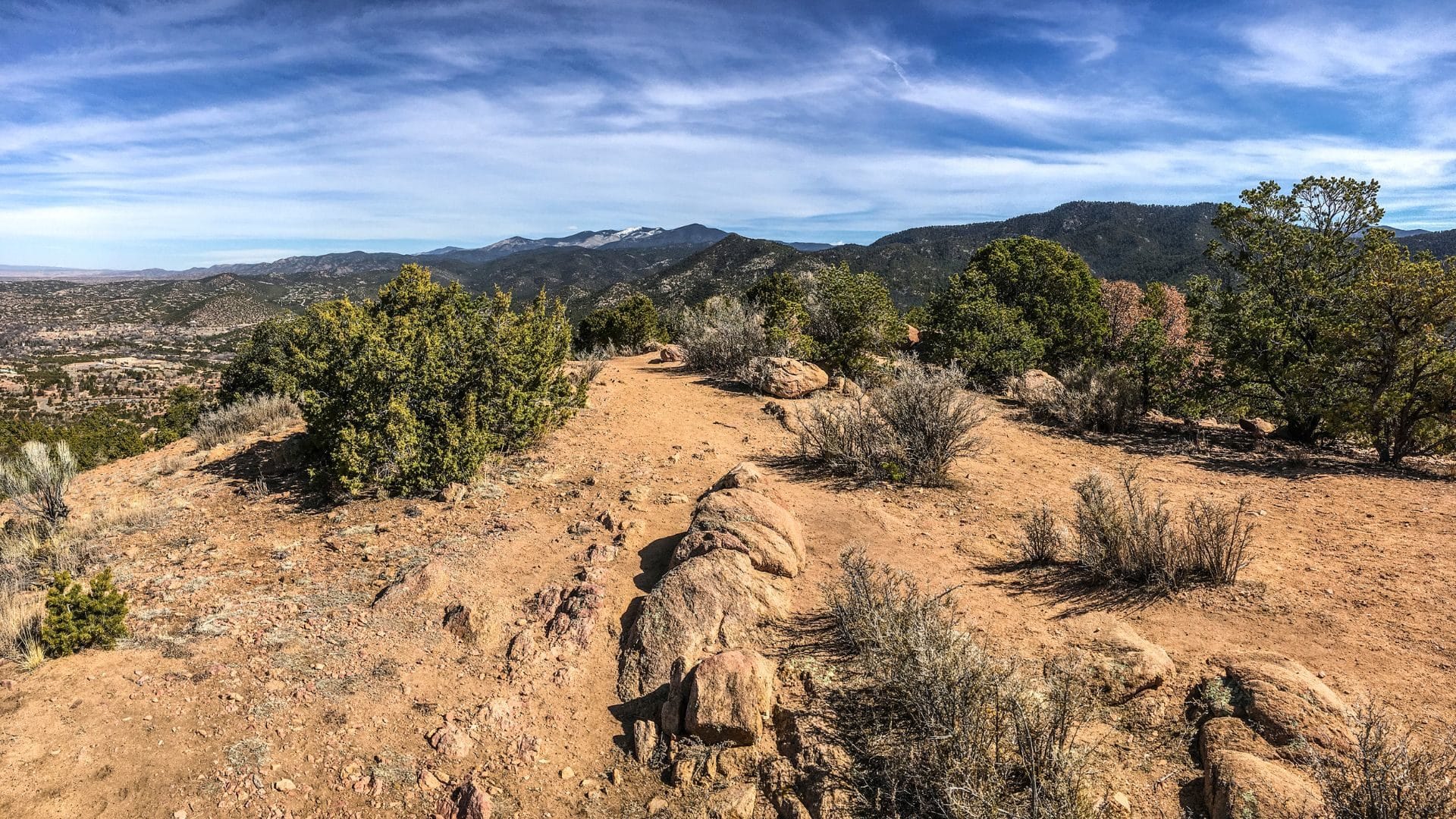 Reddish tan soil on a mountaintop in New Mexico surrounded by mountains and blue skies