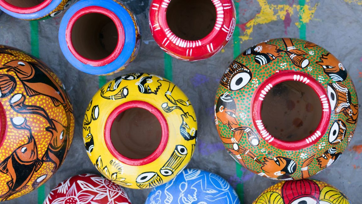 Different sized flower pots painted in bright colors with Native American patterns sitting on the concrete.