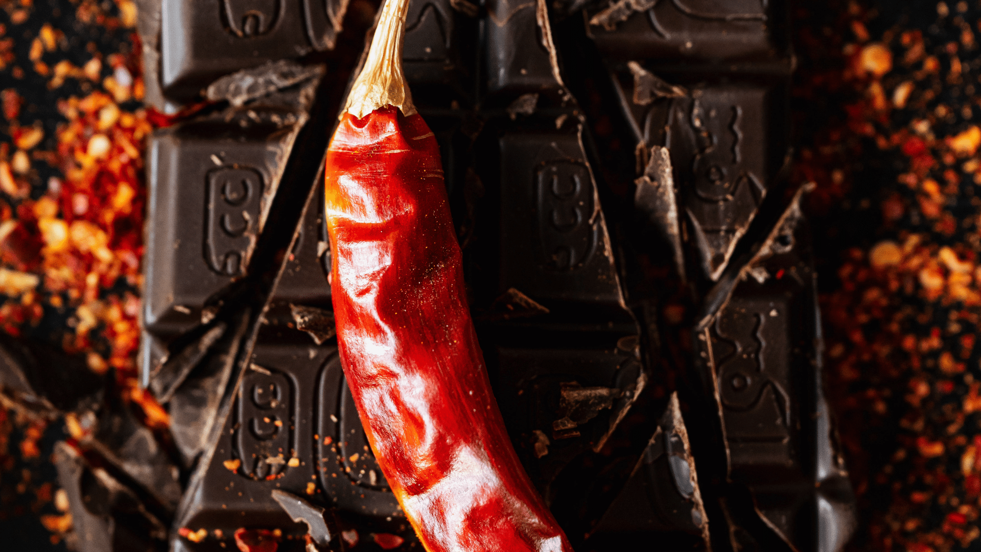 dried red chile pepper resting on dark chocolate squares with scattered spice flakes