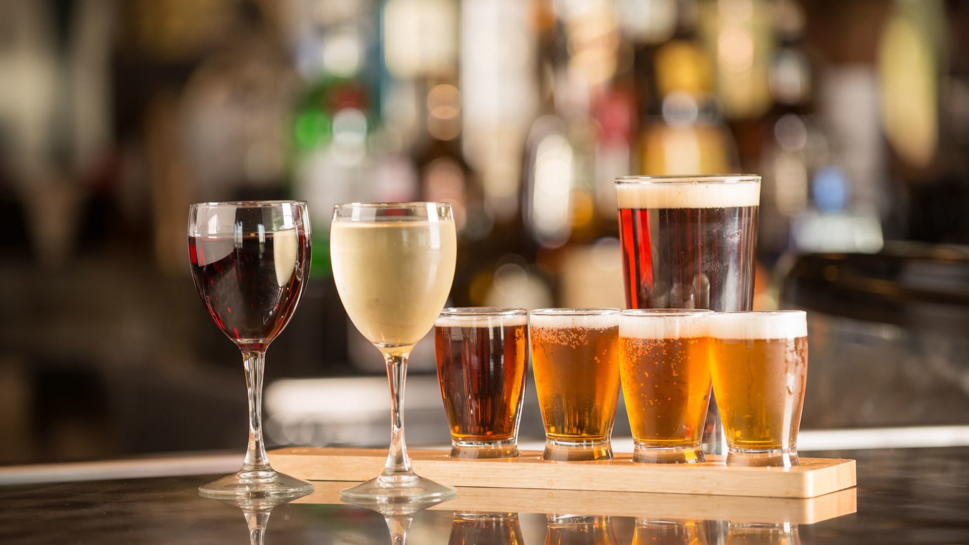 Bar top with a glasses of red and white wine, beer, and a beer flight.