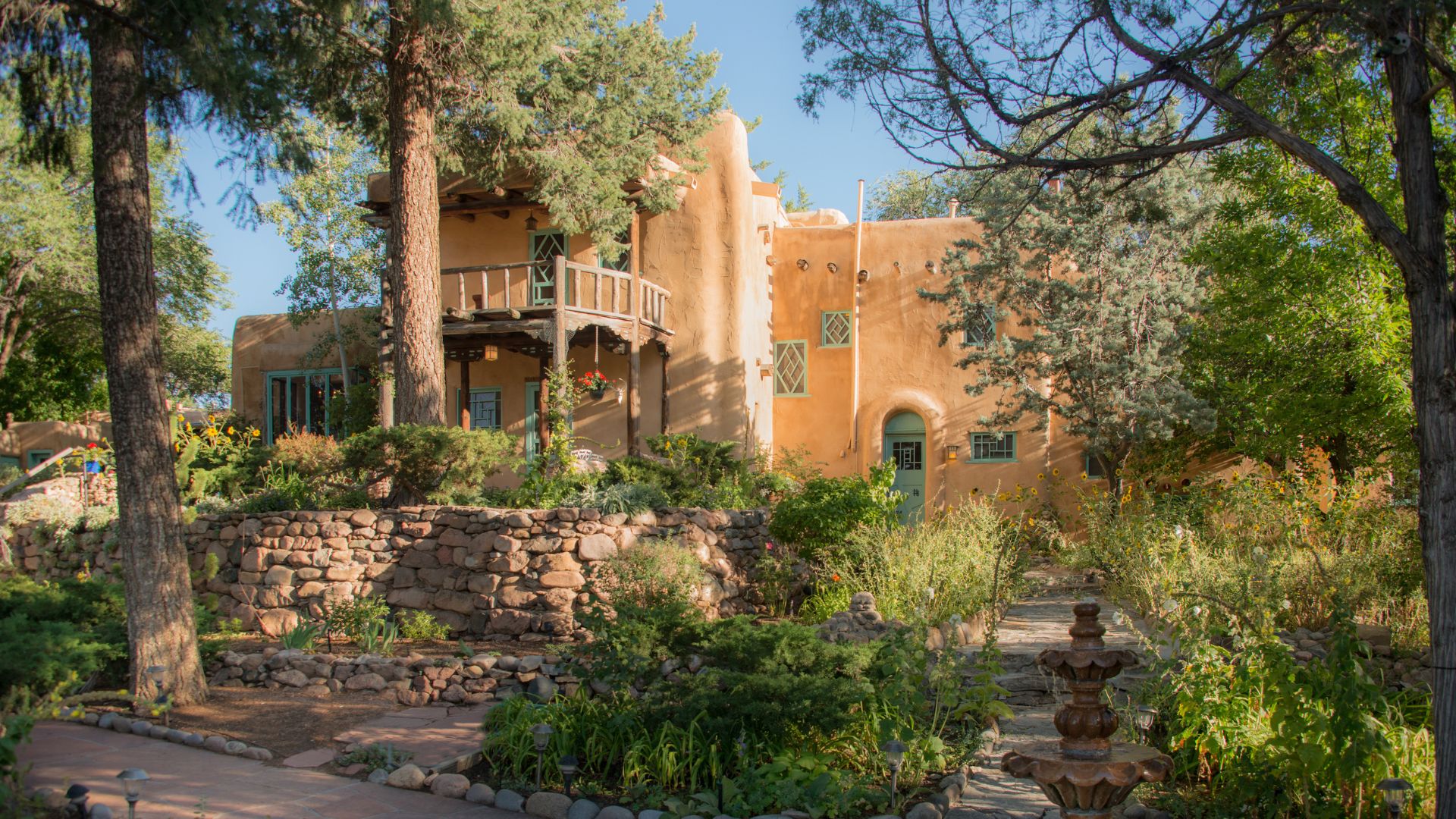 Exterior view of Inn of the Turquoise Bear, clay adobe with turquoise trim and 2nd floor balcony surrounded by lush landscaping