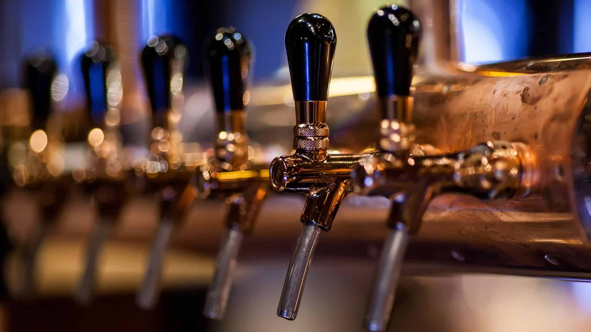 Row of silver beer taps with black handles.