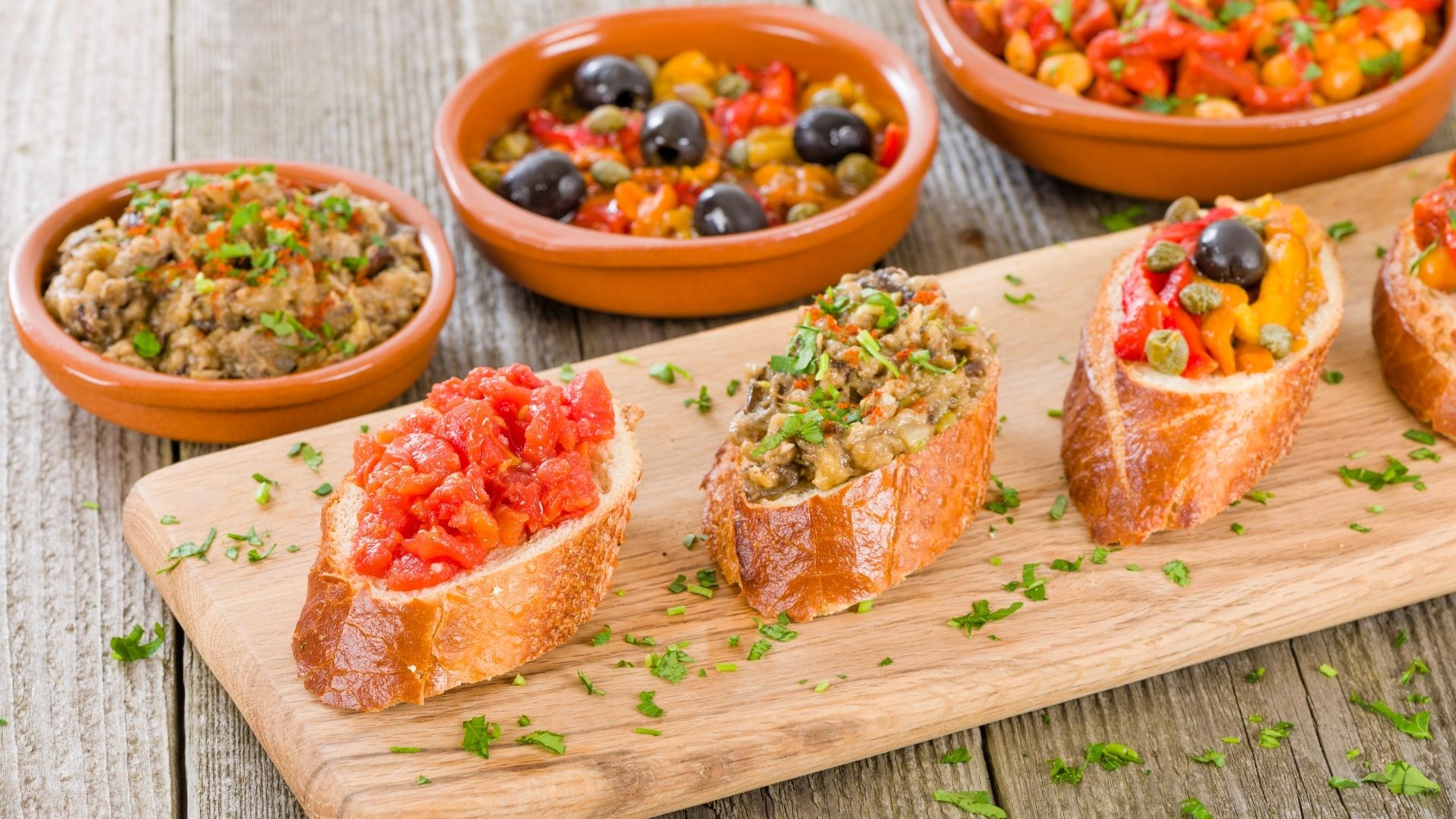 Rustic table topped with bowls and board full of breads, relishes and sauces