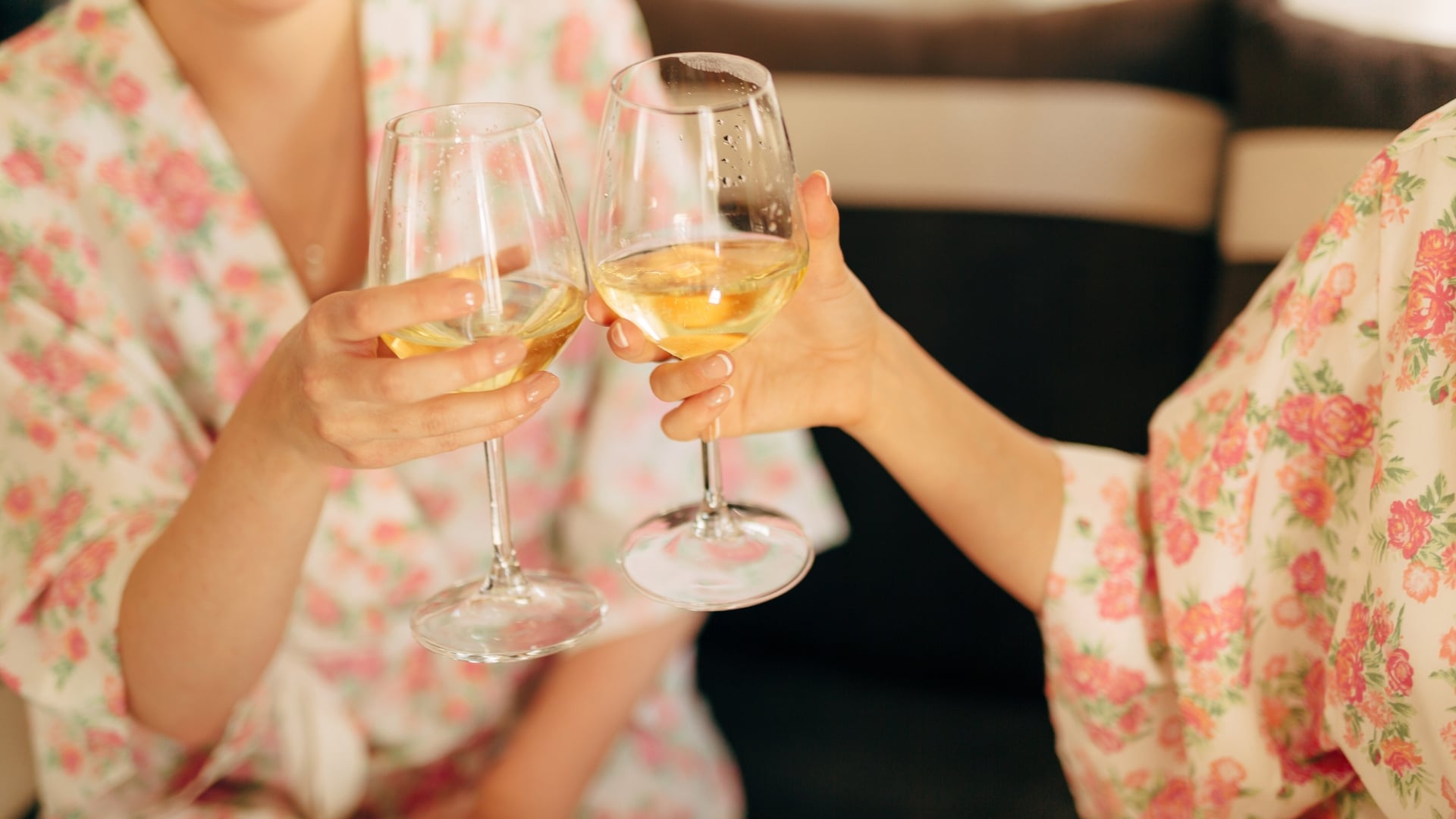 Up close of two girls in bright floral robes while clinking wine glasses