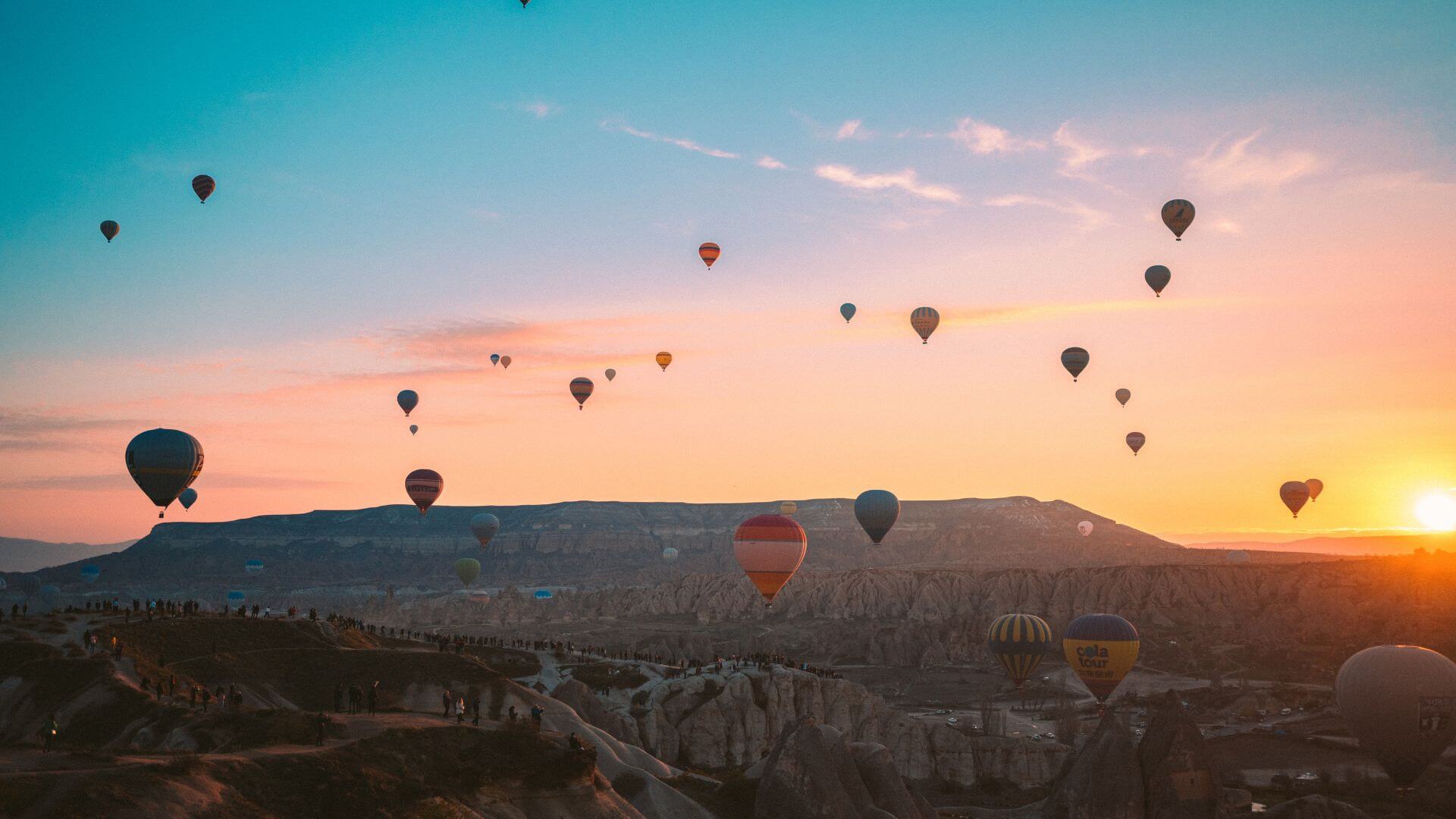Hot air balloons float over a desert landscape at sunrise.