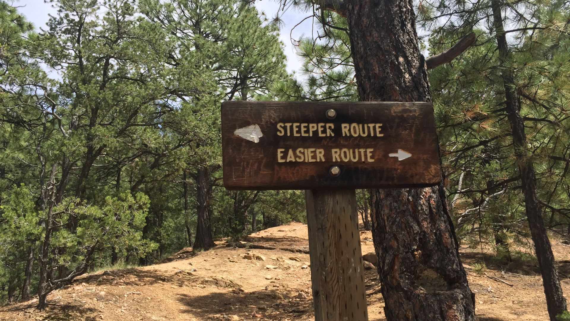 Dirt trail in Santa Fe with wooden directional sign for steeper route and easier route.