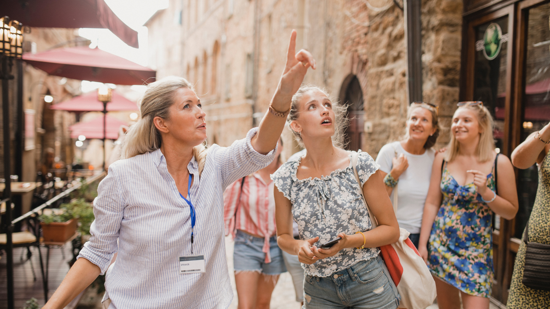 tour guide pointing while leading a group of women on a walking tour in a historic town with stone buildings and outdoor cafes 