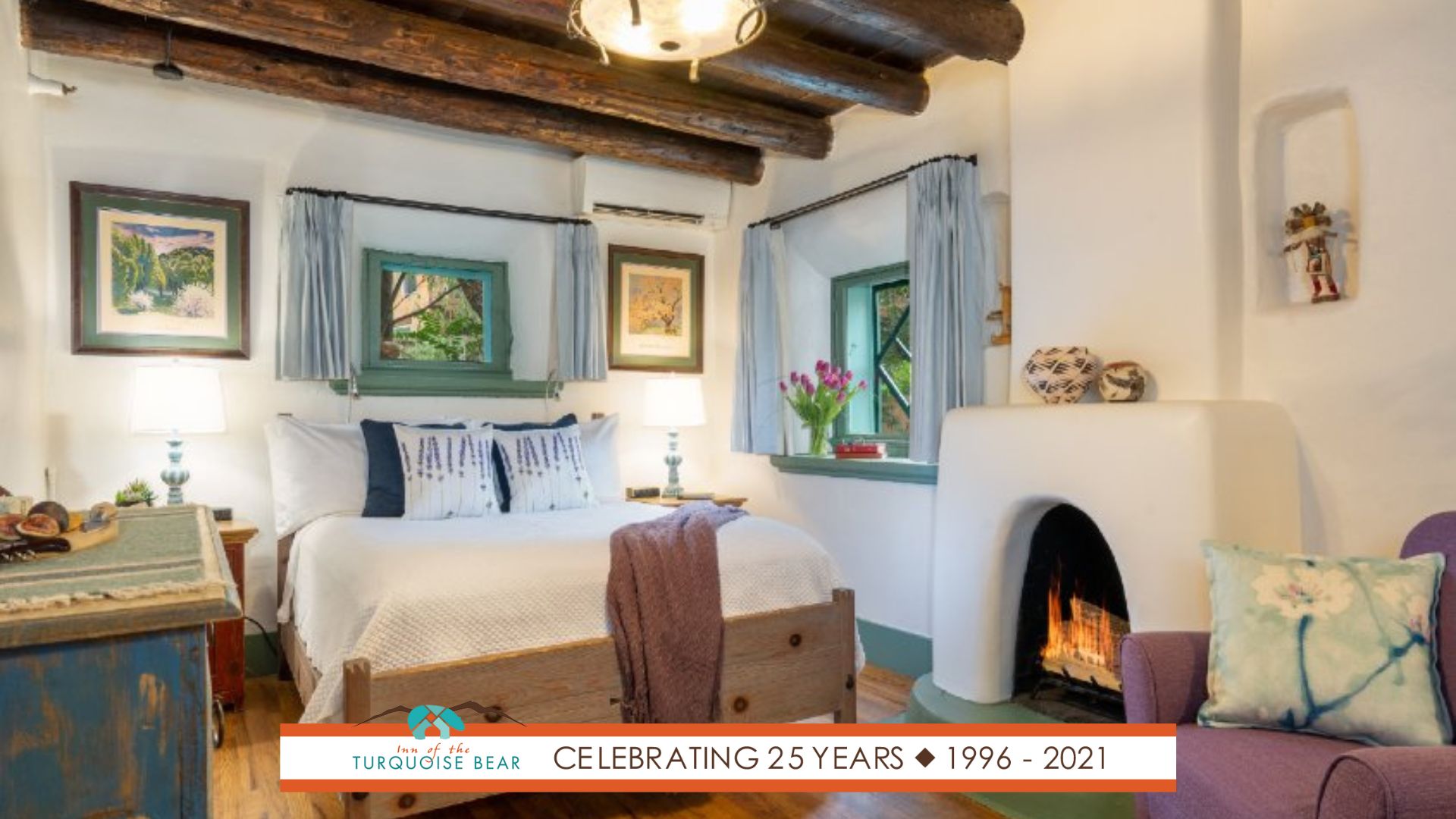 Creamy white guest room with wood beams, wood floors, Kiva fireplace, and beautiful art.