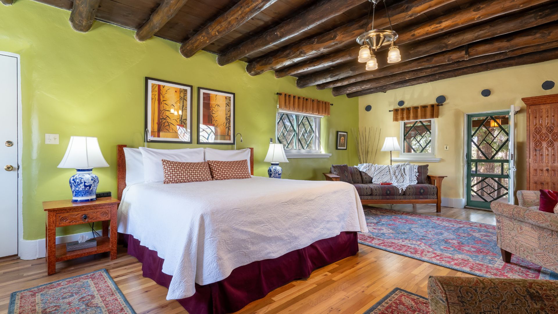 Spacious bright light green guest rooms with exposed beams, wood floors and king bed.