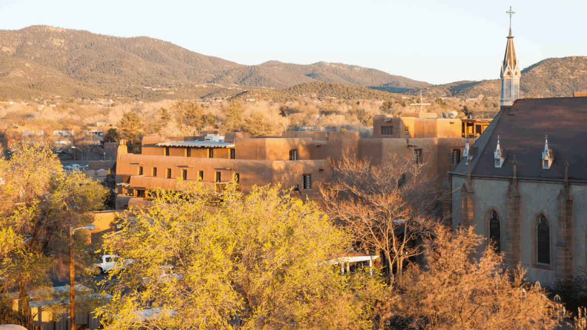 adobe style buildings and a church with mountains in the background bathed in warm sunset light