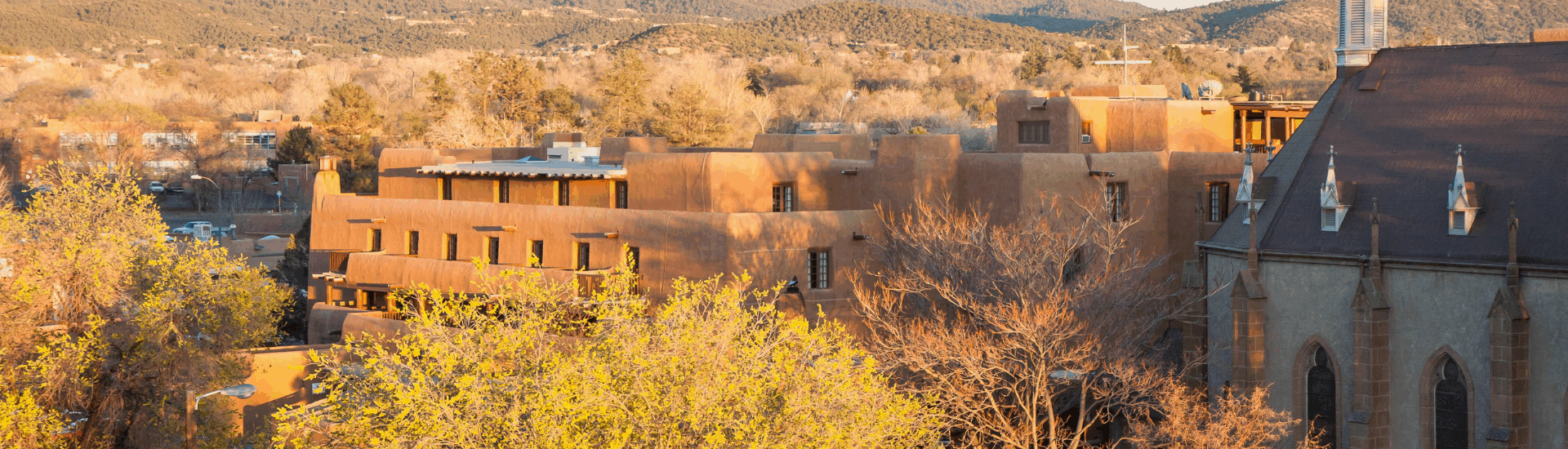 adobe style buildings and a church with mountains in the background bathed in warm sunset light