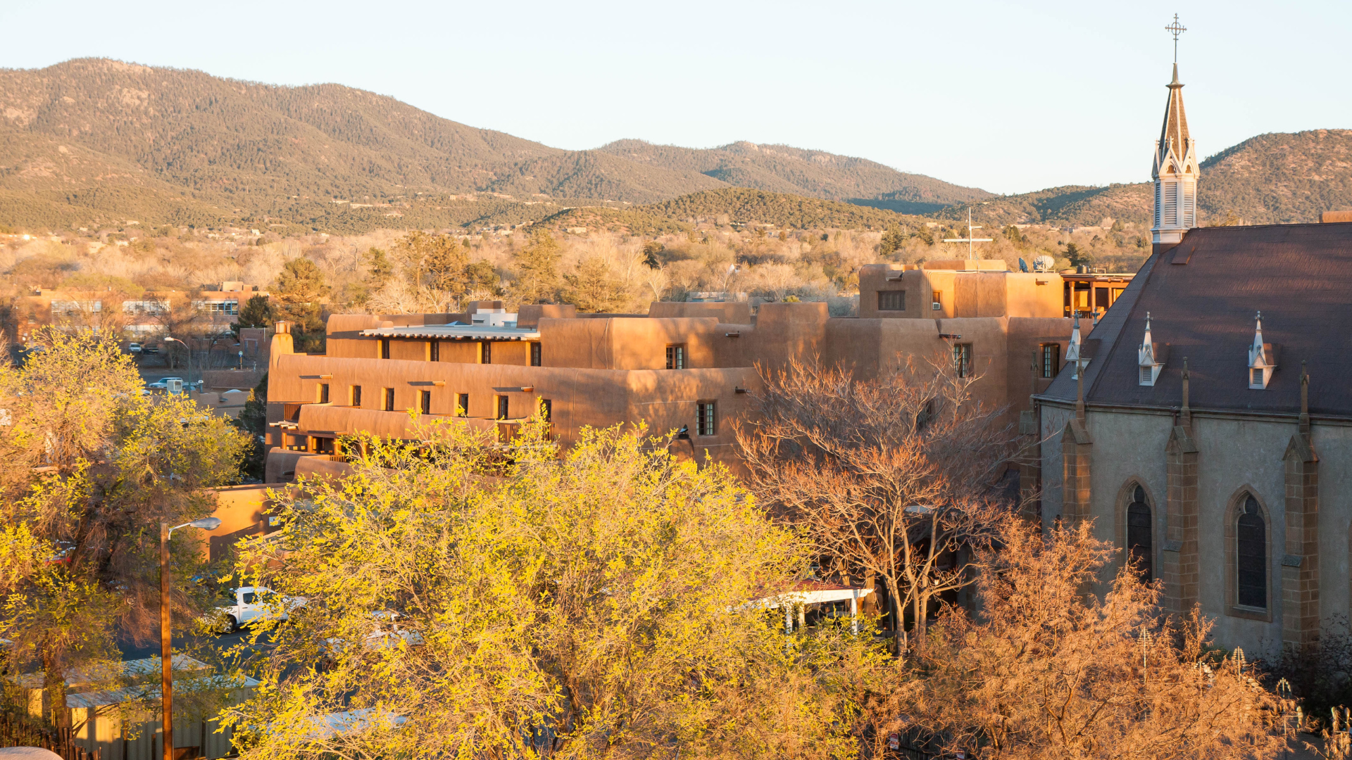 adobe style buildings and a church with mountains in the background bathed in warm sunset light