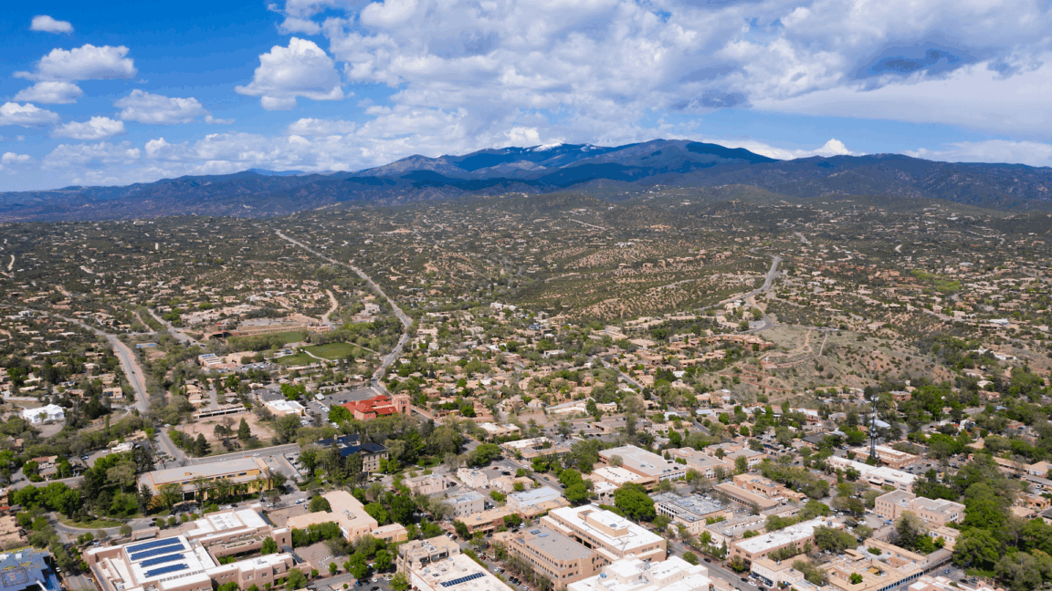 view of santa fe new mexico, with a mix of adobe-style buildings desert and surrounding mountains under a partly cloudy sky