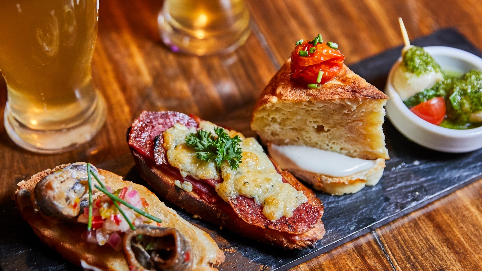 A closeup of a lineup of Spanish tapas with two beers glasses in the background