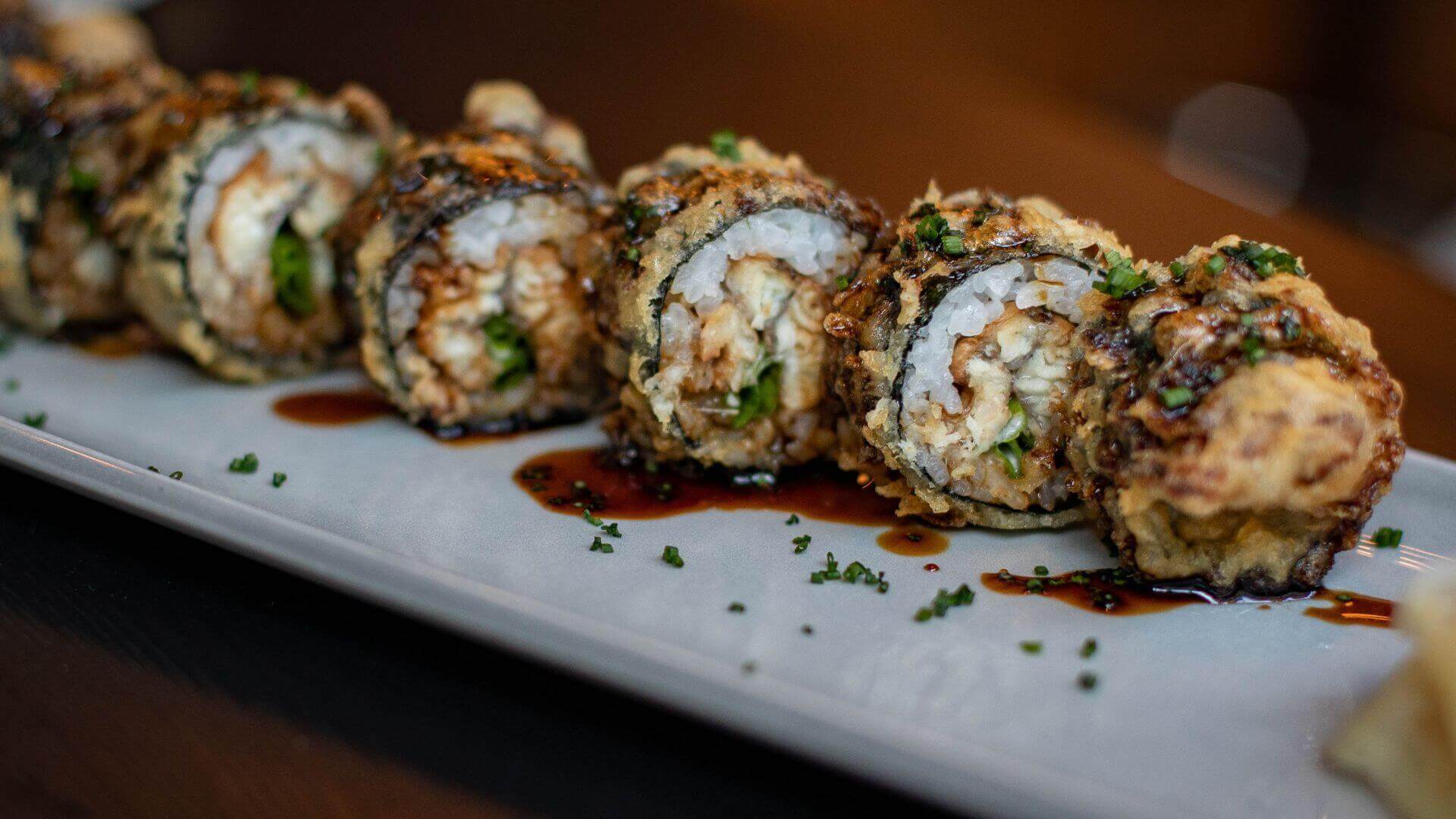 crispy sushi rolls with rice seafood and herbs drizzled with sauce on a white plate