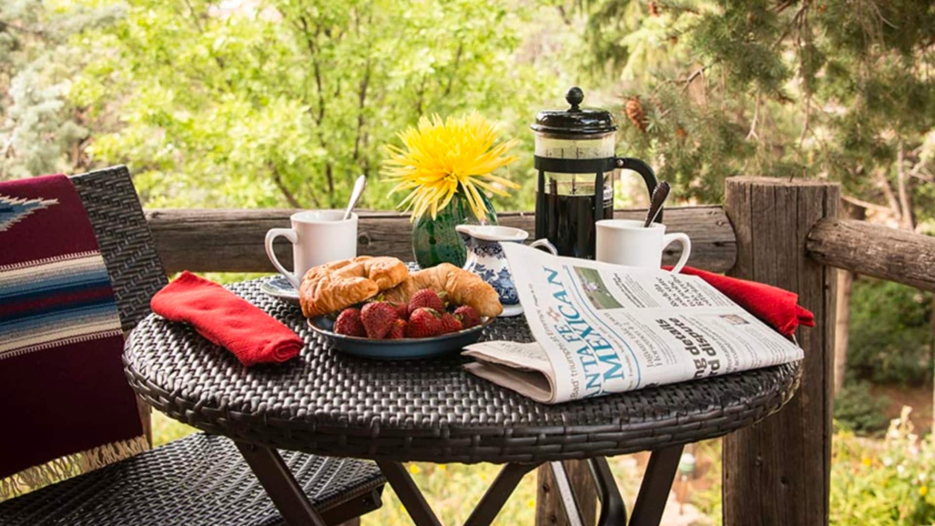 A patio table at Inn of the Turquoise Bear with coffee press, baked goods, strawberries, flower vase, and a newspaper