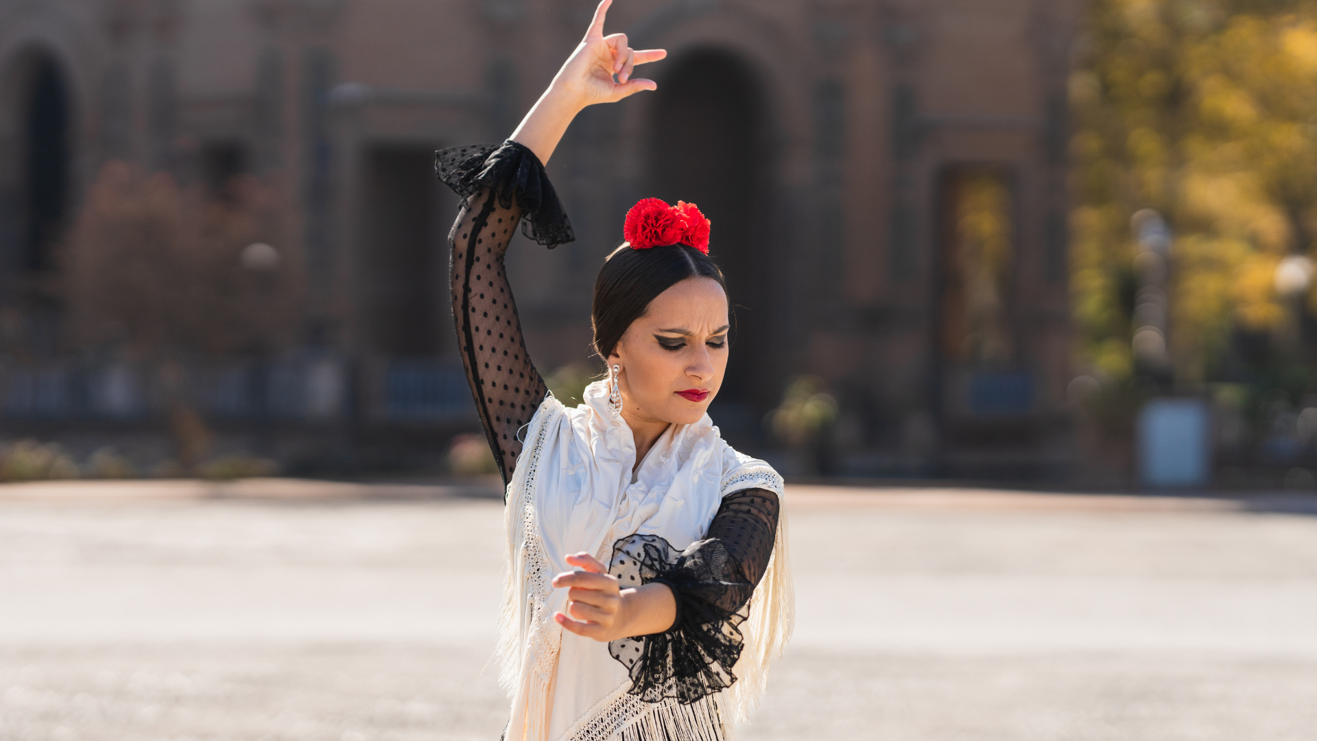 woman performing flamenco dance in traditional attire with flowers in hair and lace sleeves