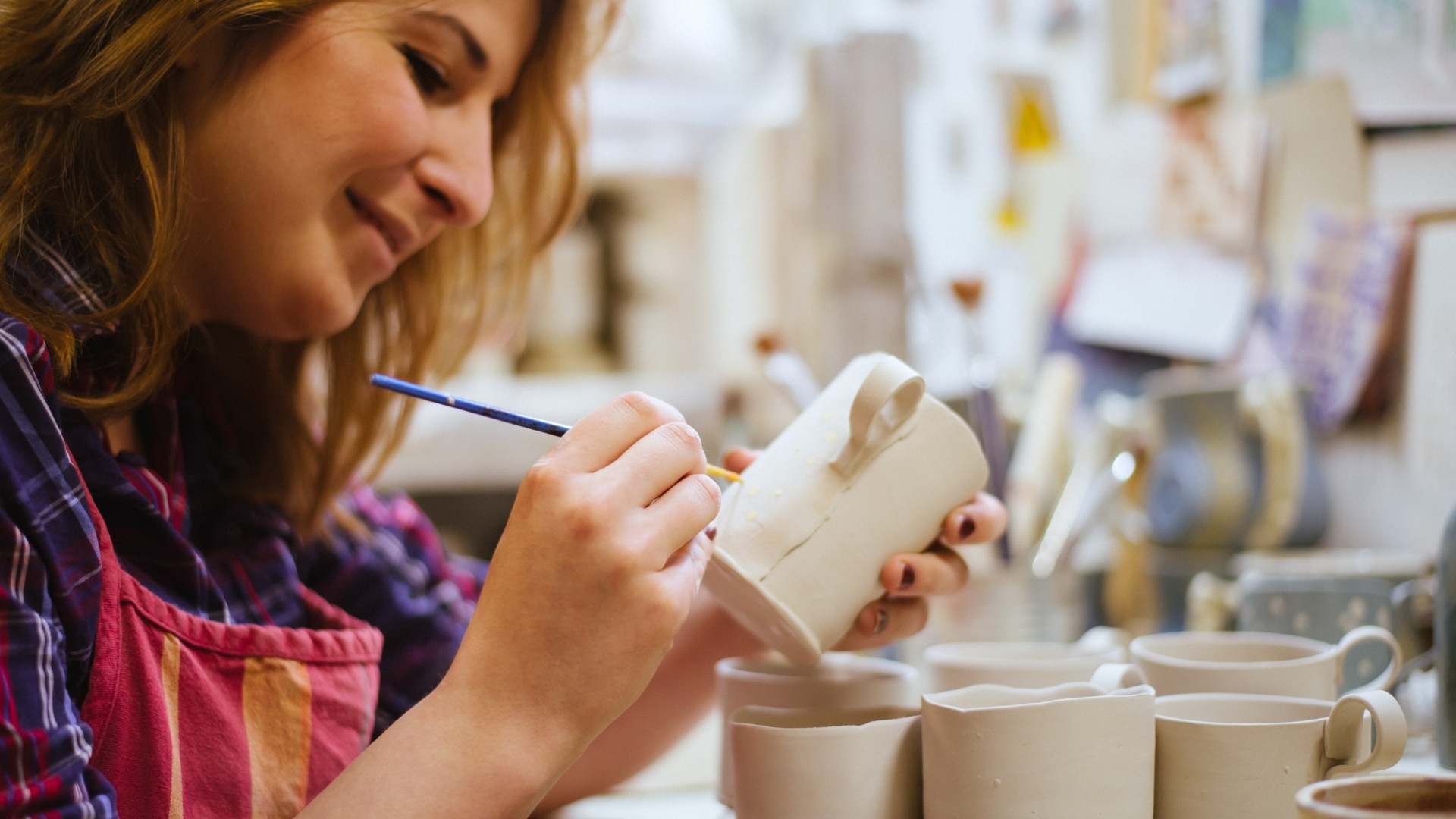 A smiling woman painting handmade mugs