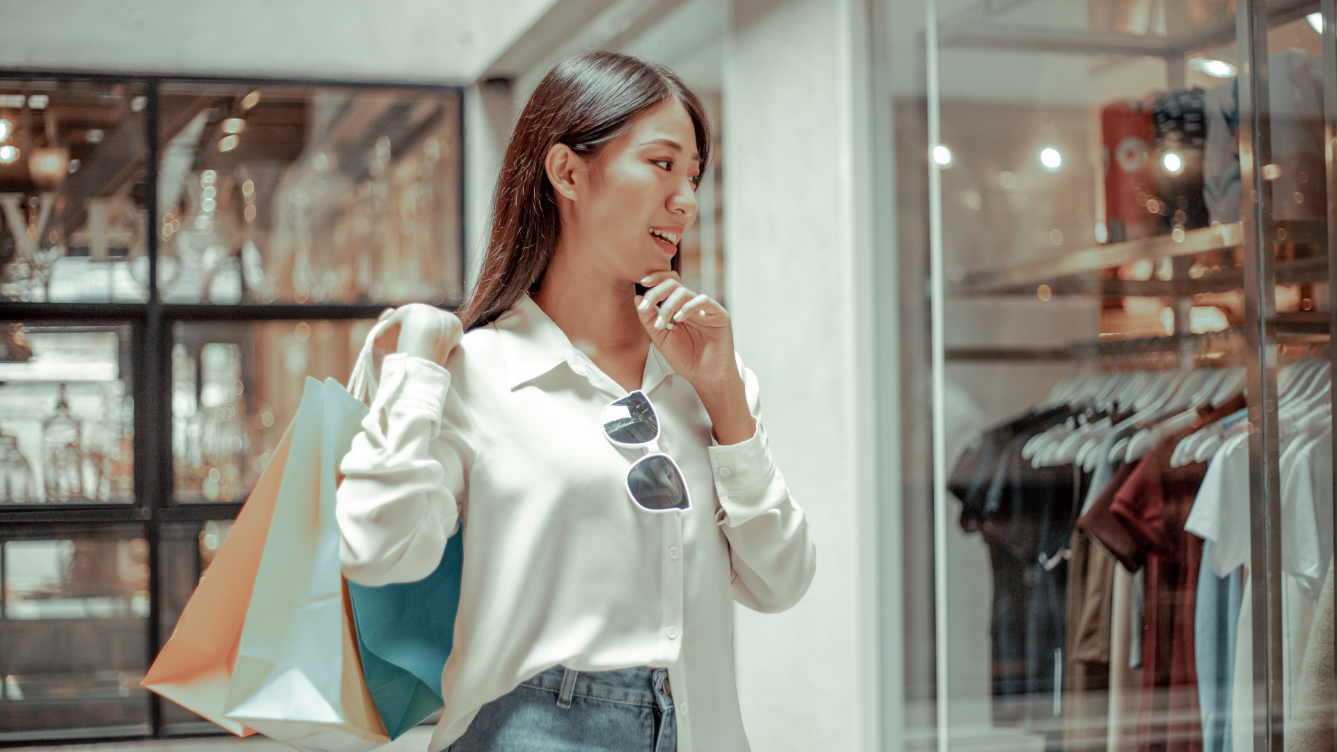 woman smiling while holding shopping bags and looking at clothing store display