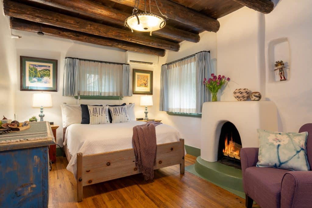 O Henry guest roomo with white walls, wood floors, Kiva fireplace and log ceiling