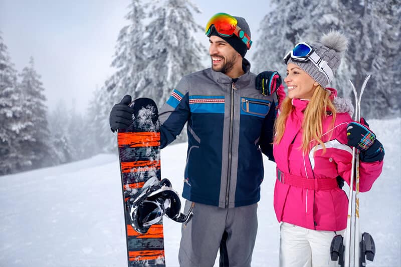 Cute yong couple in ski gear holding a snowboard and skis surrounded by snow in Northern New Mexico|Relaxing couples massage with candles|COuple with backpacks hiking on snow covered ground in Santa Fe|Cozy Southwestern bedroom with fireplace in Santa Fe