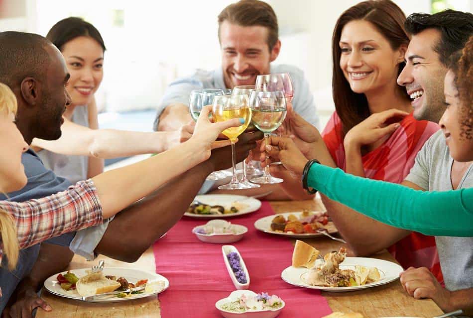 Happy group exchanging cheers over a dinner table with wine glasses.