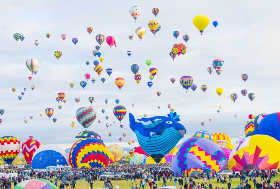 Crowd under dozens of colorful hot air balloons at Albuquerque Balloon Festival.