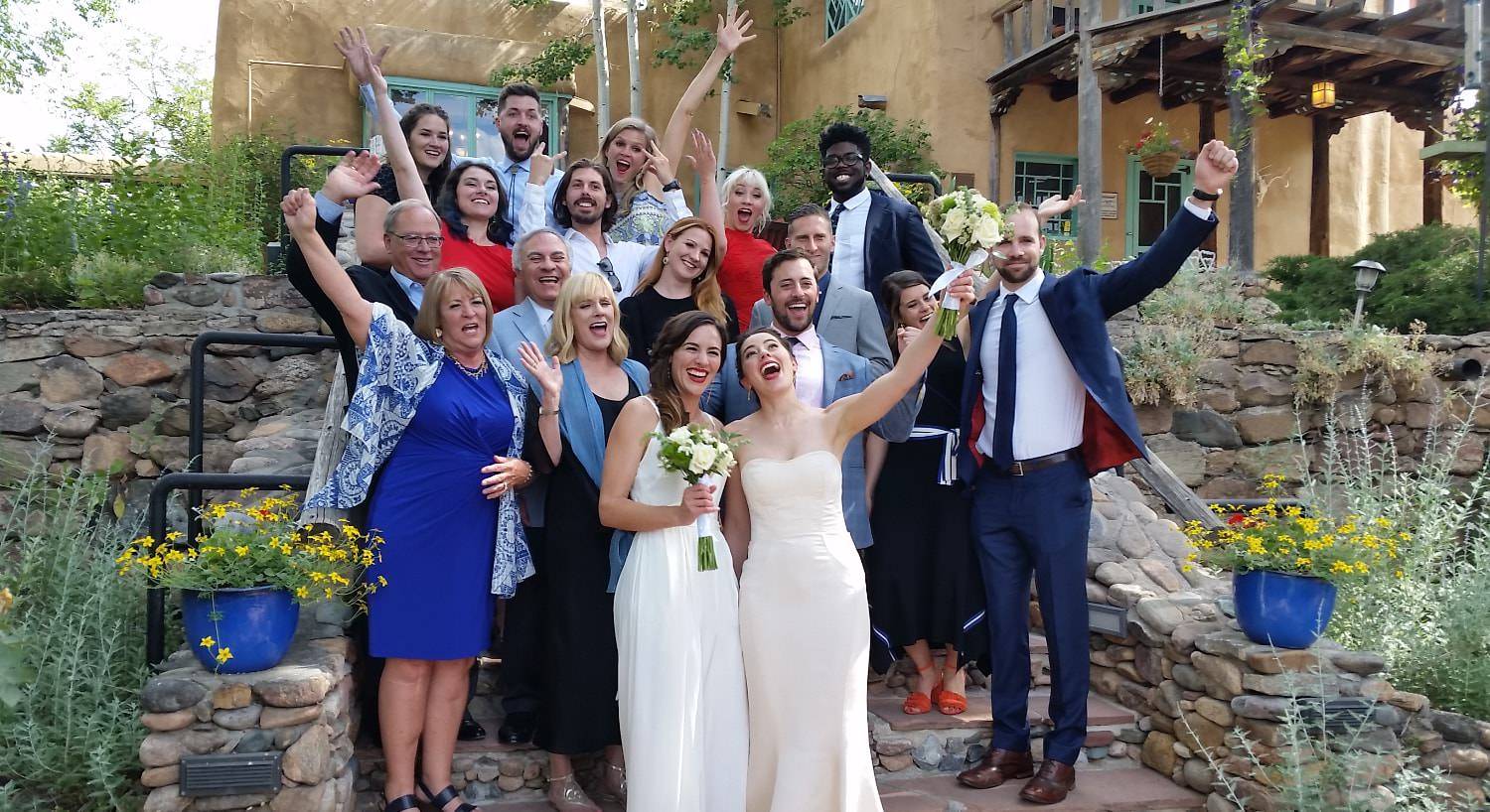 Two brides and wedding guests standing on stone steps smiling and celebrating