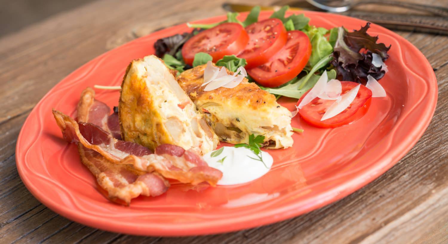 Orange plate with bacon, quiche, sliced tomatoes, and lettuce