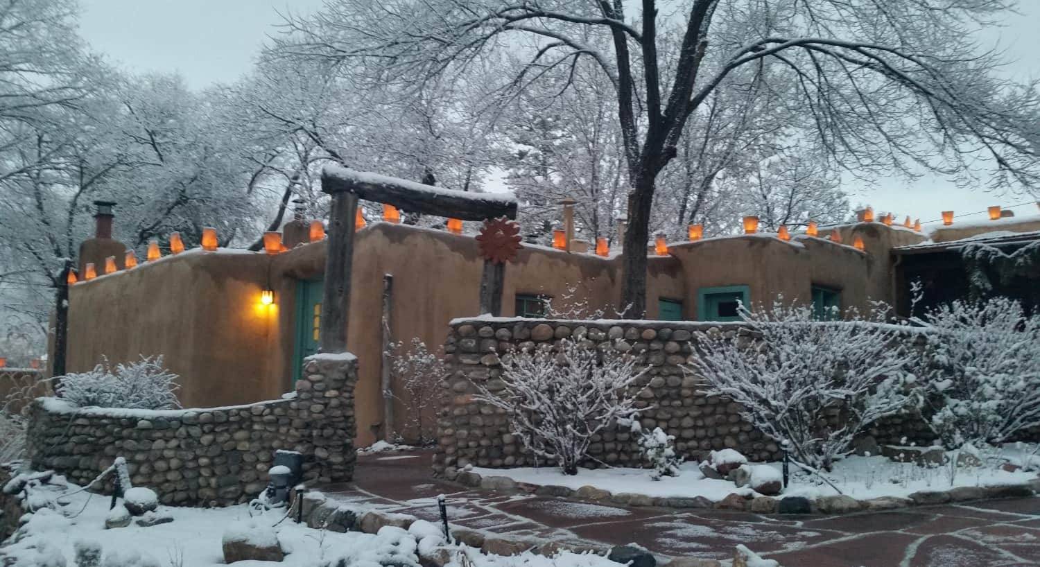 Exterior view of the property surrounded by large green trees with snow coming down, covering vegetation