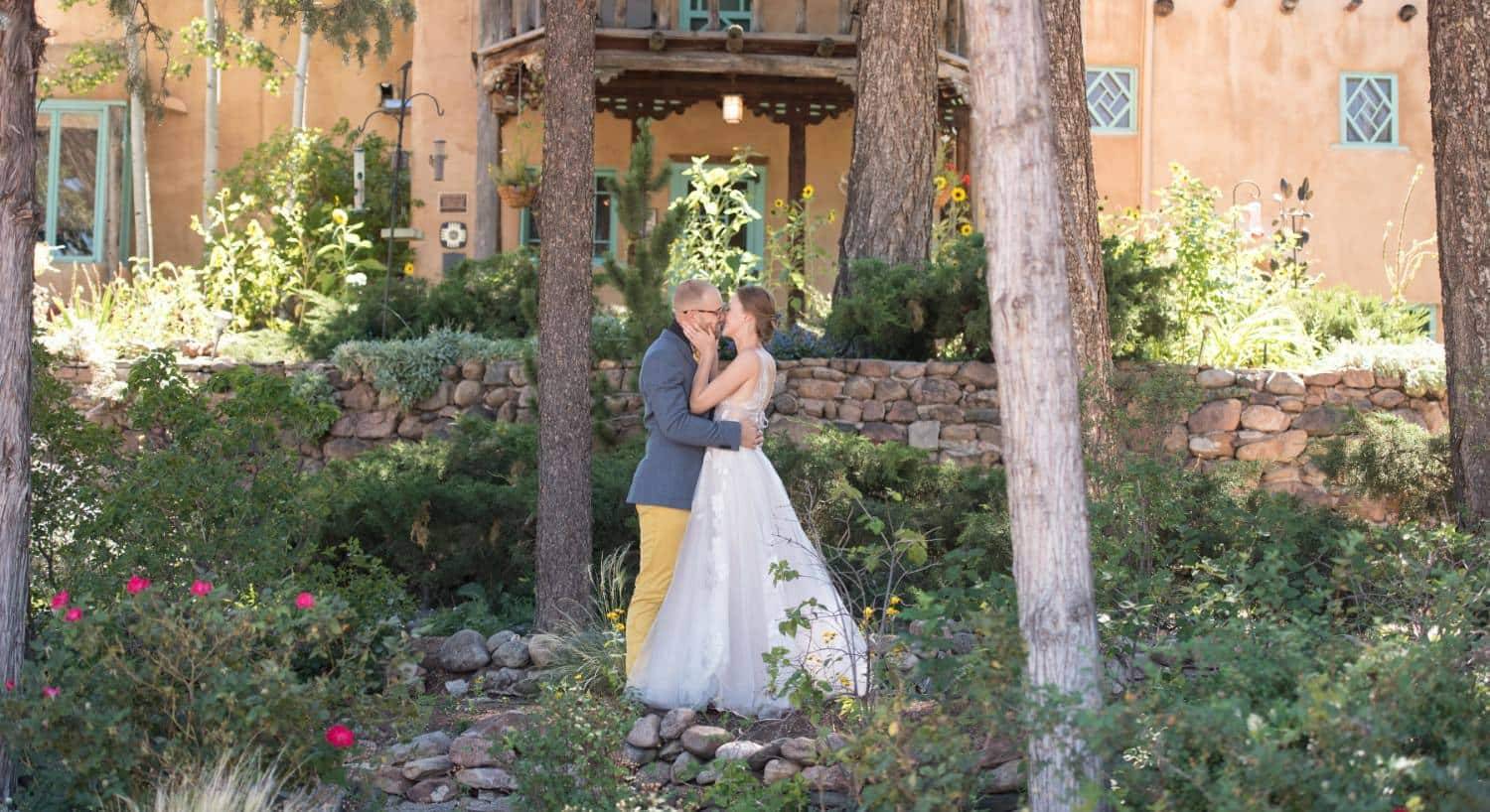 Bride and groom kissing each other standing in a garden outside of the property surrounded by green bushes and vegetation