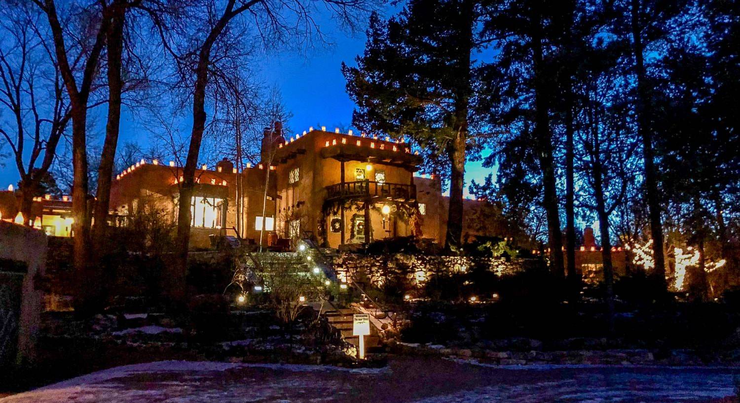 Exterior view of the property at dusk decorated for Christmas with lighted lanterns and evergreen draped on the patio