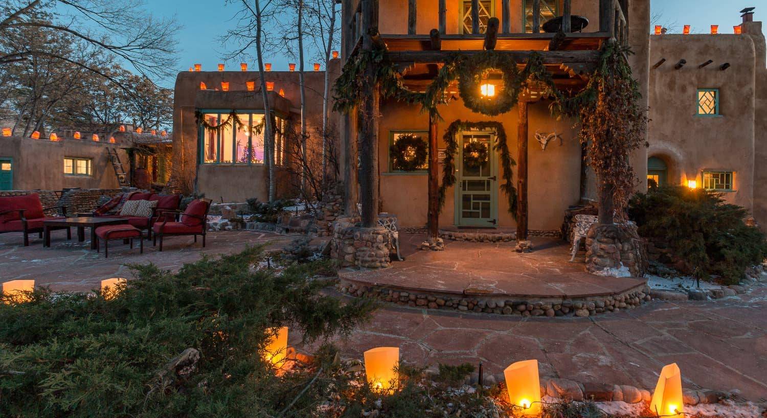 Exterior view of the property at dusk decorated for Christmas with lighted lanterns and evergreen draped on the patio