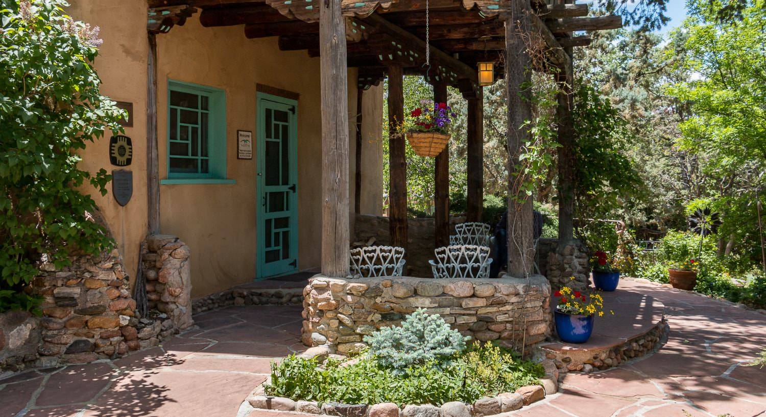 Exterior view of the property with a patio, flower gardens, and large green trees