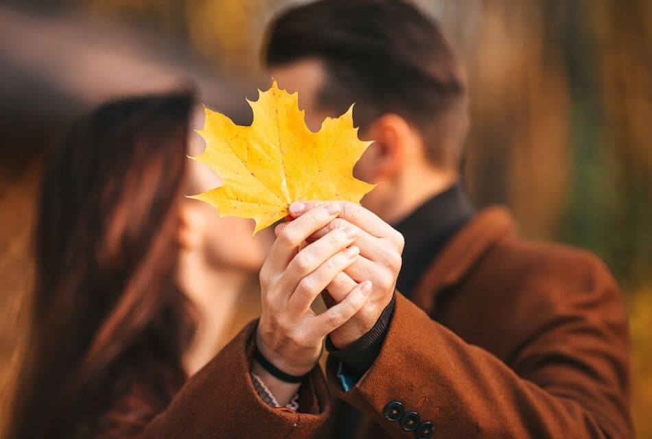 Couple kissing behind a yellow autumn leaf